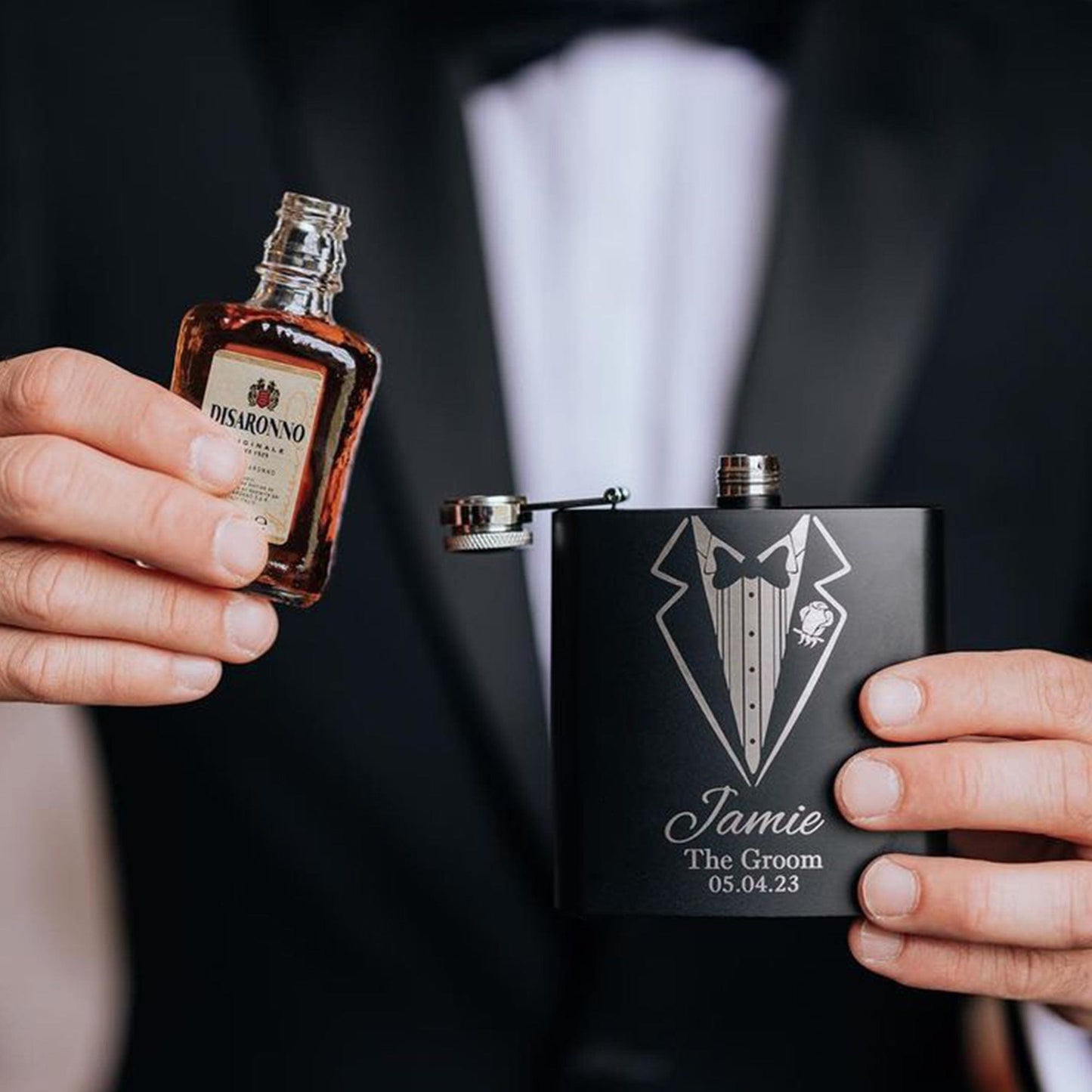 a man wearing a tuxedo whilst holding a hip flask pooring his drink into the flask, the flask is engraved the recipients name,role and date of the wedding. The perfect groomsman gift