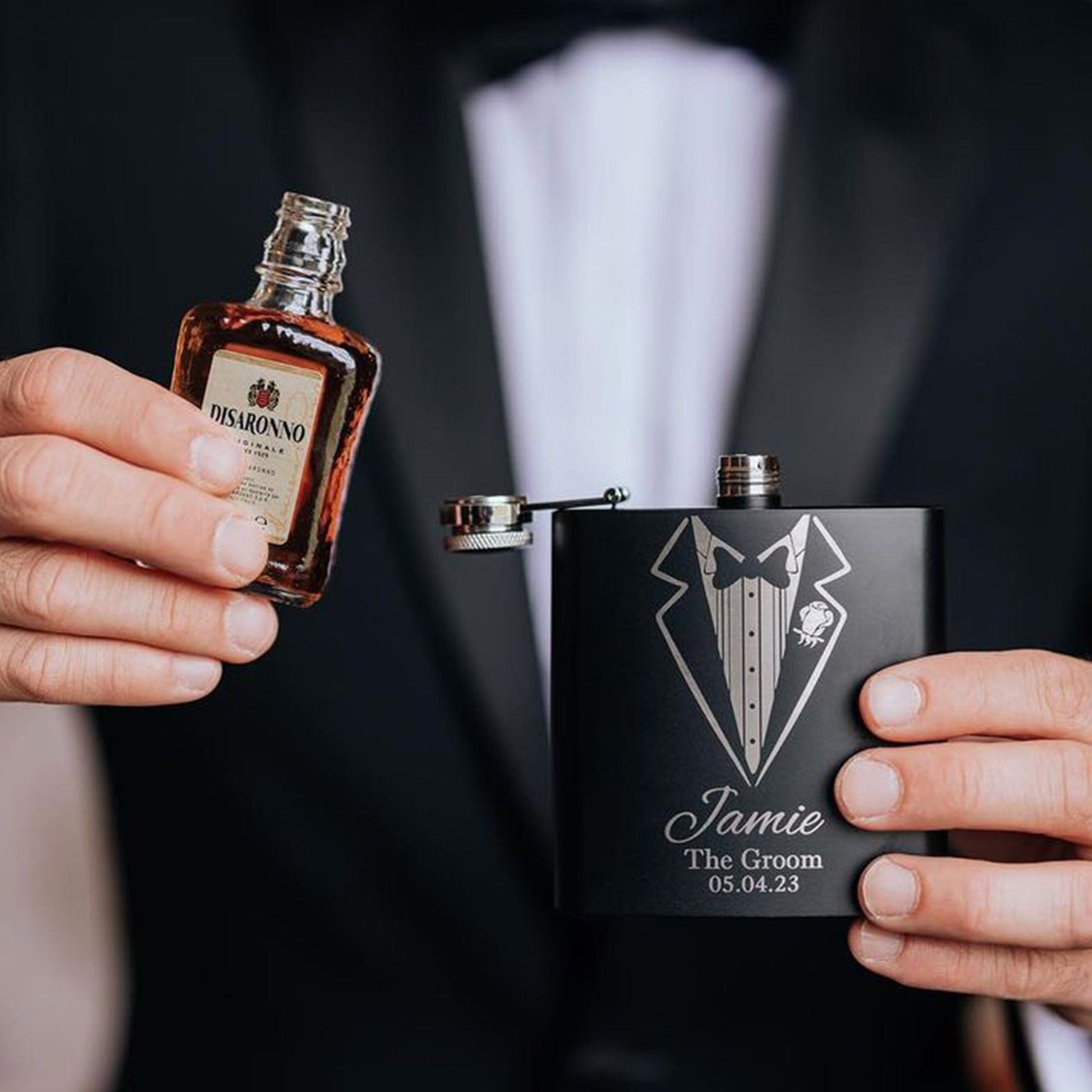 a man wearing a tuxedo whilst holding a hip flask pooring his drink into the flask, the flask is engraved the recipients name,role and date of the wedding. The perfect groomsman gift
