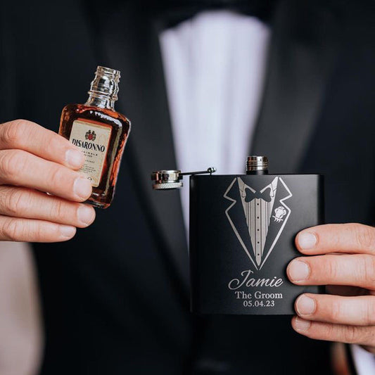 a man wearing a tuxedo whilst holding a hip flask pooring his drink into the flask, the flask is engraved the recipients name,role and date of the wedding. The perfect groomsman gift