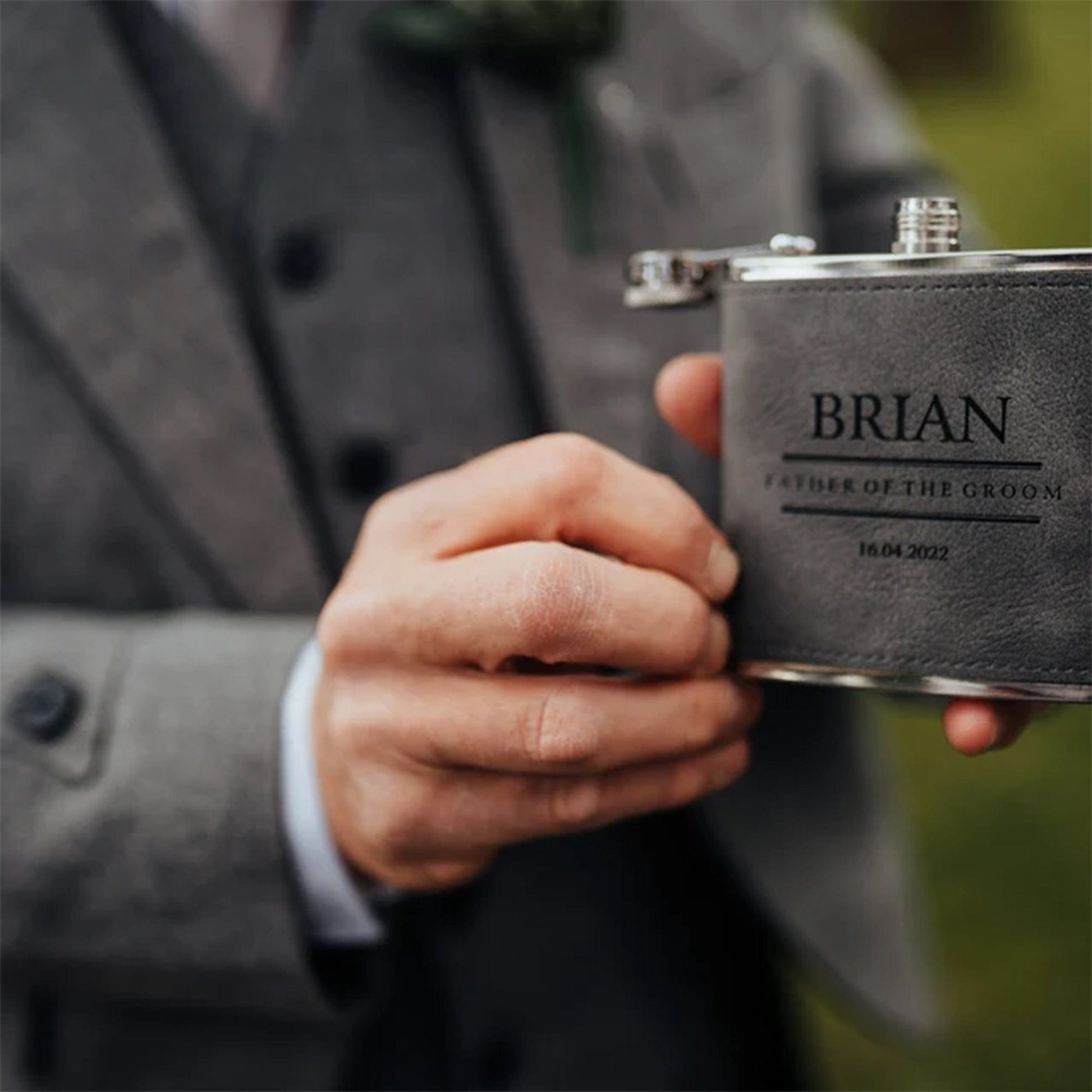 a set of three flasks all side by side one black, one grey, one brown all with a traditional design on the front with the recipients names, role and the wedding date all laser engraved. the perfect wedding groomsman gift.