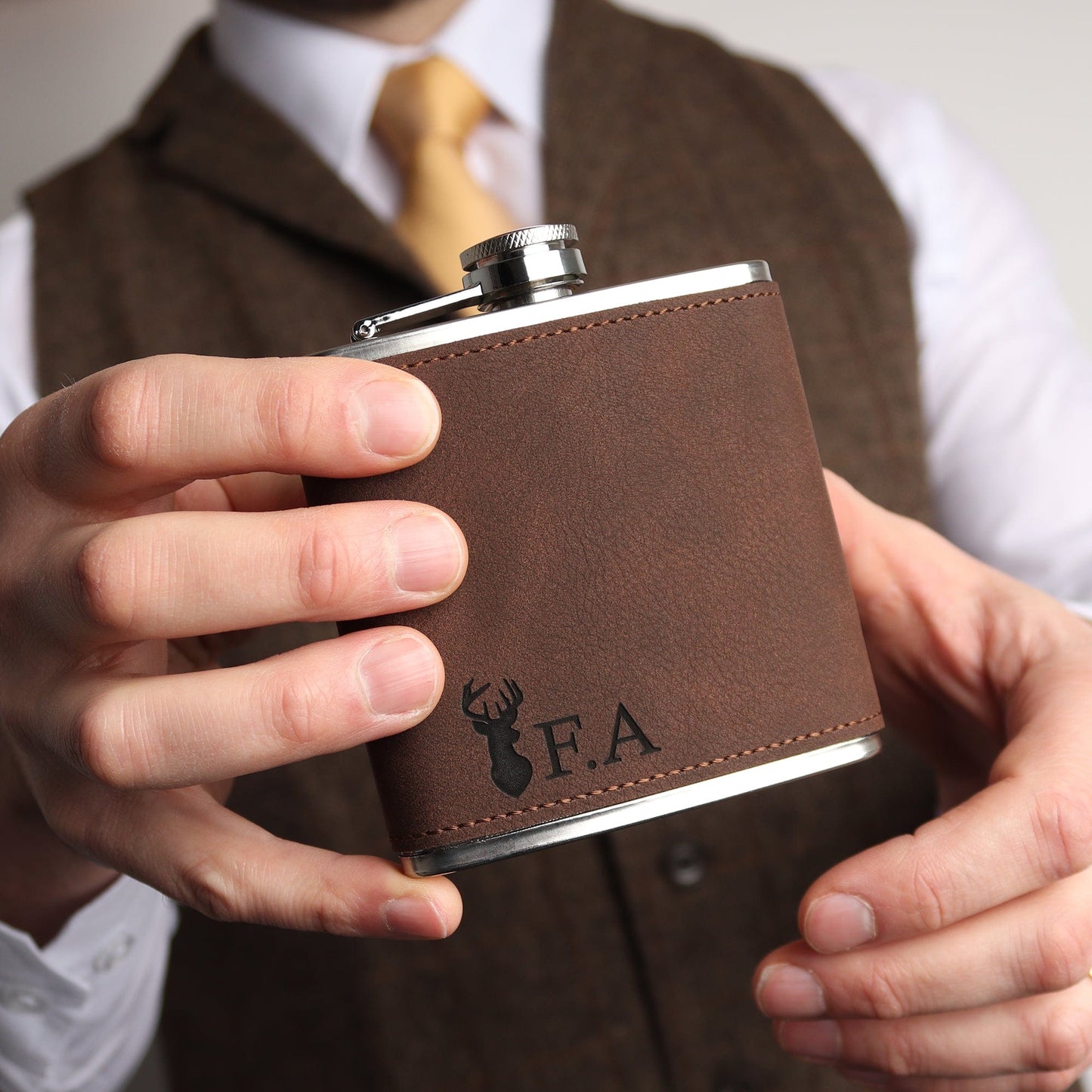 Picture of a 6oz stainless steel groomsmen hip flask wrapped in a brown soft leather look material. The flask can be engraved with any Initials. The flask has a small stag head engraved to the bottom left corner. engraving comes through as black.