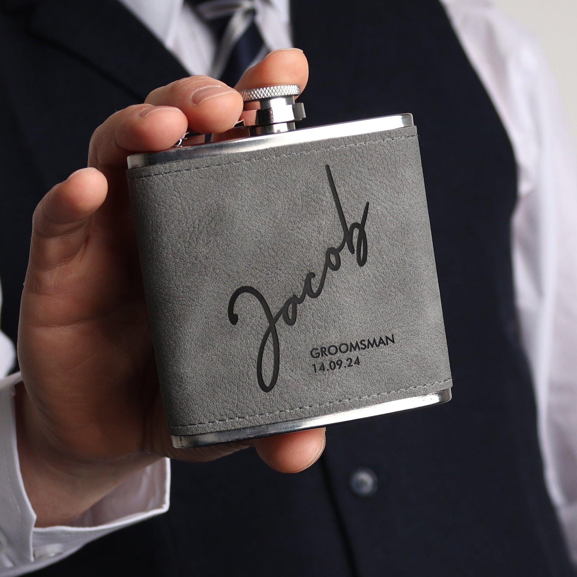 Picture of a 6oz stainless steel groomsmen hip flask wrapped in a grey soft leather look material. The flask can be engraved with any role, name and date. The engraving comes through as black