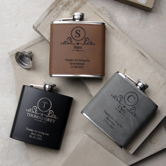 a set of three flasks all side by side one black, one grey, one brown all with a traditional design on the front with the recipients names, role and the wedding date all laser engraved. the perfect wedding groomsman gift.