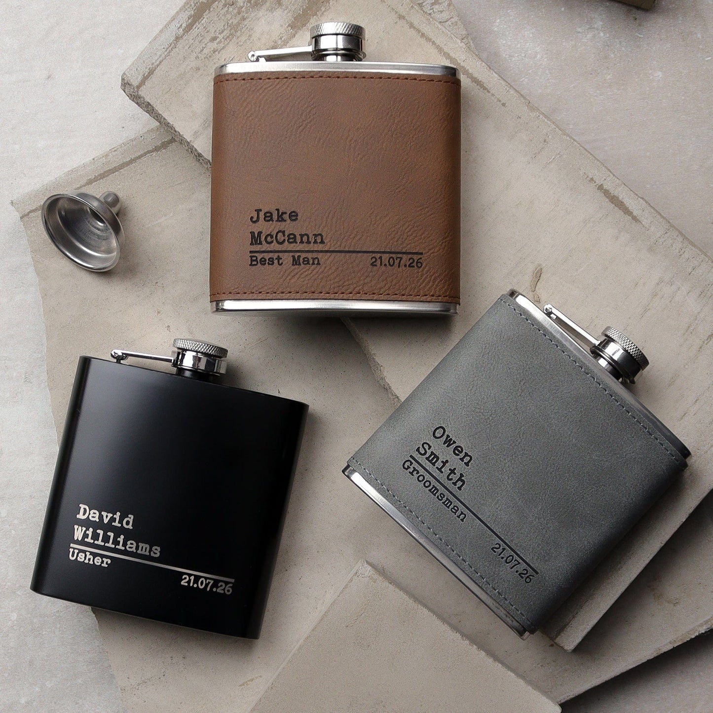 a classic leather hipflask lay on a chesterfield sofa with a union jack cushion underneaath it, the flask is lasered with the groomsmennames, role and dates creating the perfect groomsman gifts