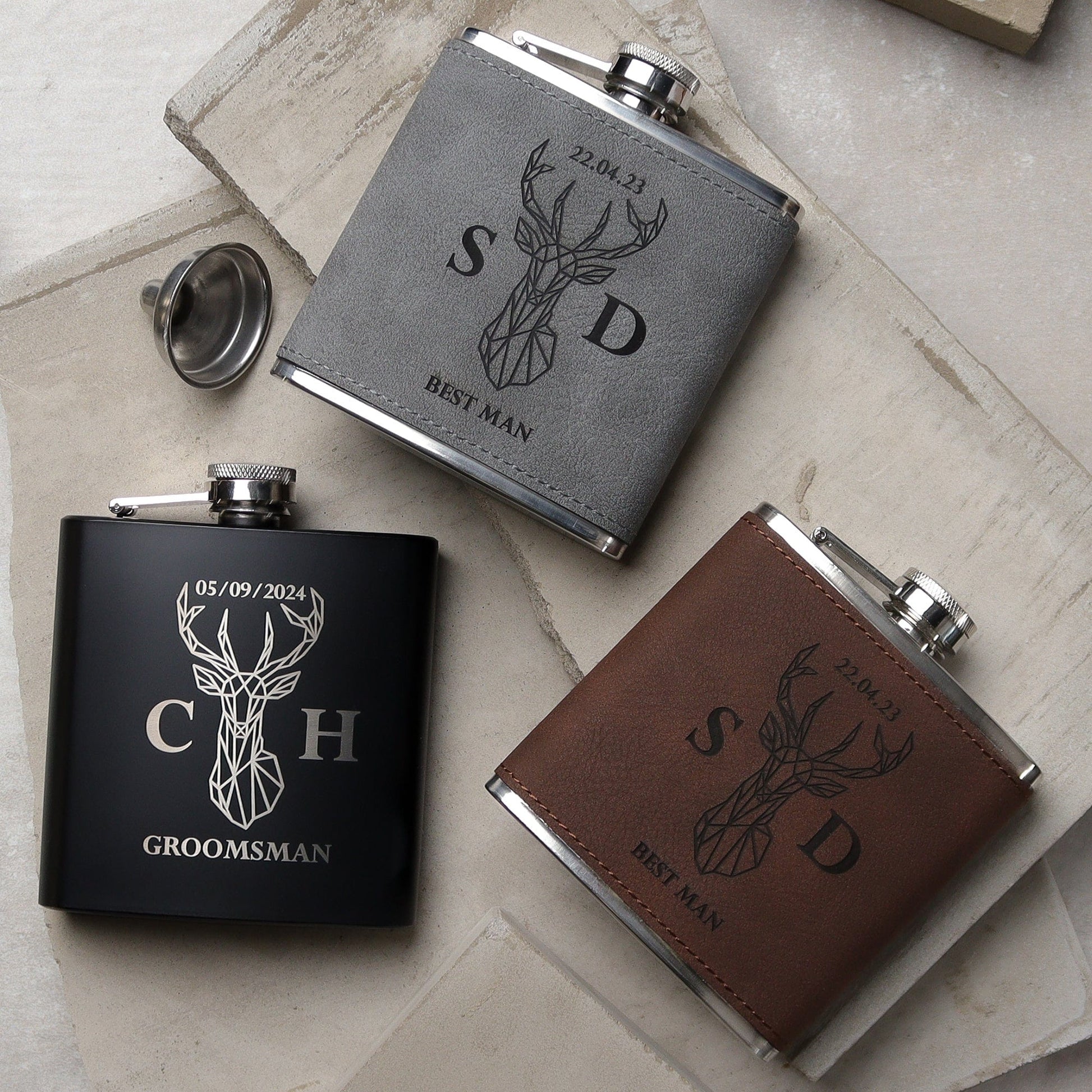 Set of three flasks all side by side one black, one grey, one brown all with a traditional design on the front with the recipients names, role and the wedding date all laser engraved. the perfect wedding groomsman gift.